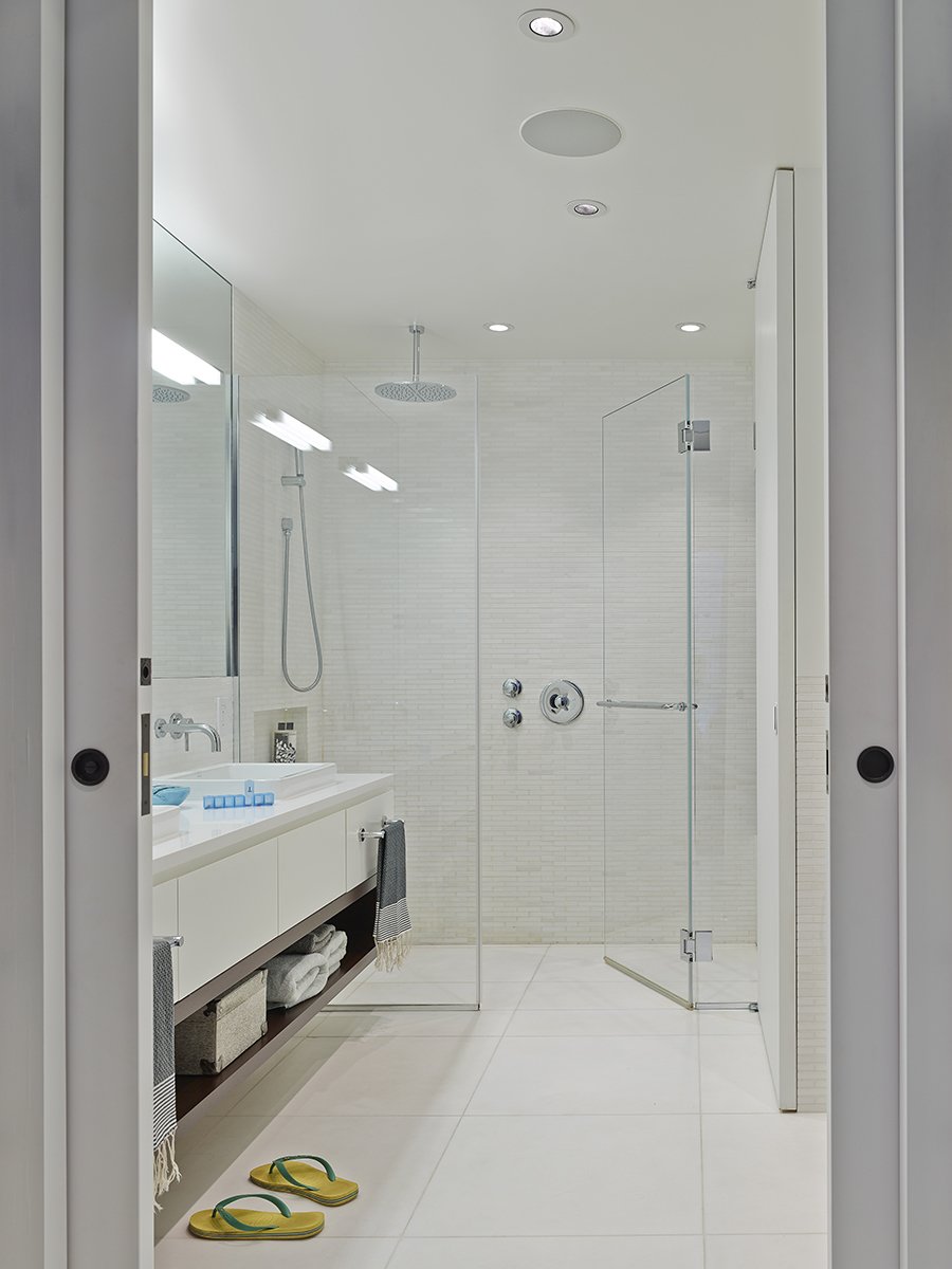 White Thassos floor and wall tile from thassos.com lines the bathroom surfaces. The vanity is custom, the sink and shower faucets are from Lacava, and the sink is Decolav. Photo by Frank Oudeman.