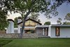 The home's outer walls were dry-stacked with limestone cut from a Texas Granbury quarry, and its gabled roof was made with weathered Cor-Ten steel that emits the same maverick spirit as a Richard Serra sculpture. The freestanding fireplace just inside the courtyard was even salvaged from the old house’s living room. Clean stucco walls contrast with the grass and trees, while reclaimed wood siding complement them. Photo of Preston Hollow modern home
