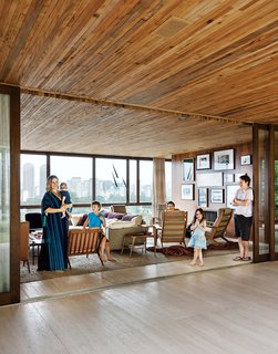 São Paulo architect Isay Weinfeld's Casa Deck offers cinematic vistas, a lush garden, and a retreat from Brazil's largest city. With São Paulo on one side and a terrace and garden on the other, the Strozenbergs’ living room feels vast. The sofa is a Harry Large by Antonio Citterio for B&B Italia and the coffee table behind Ticiana Strozenberg (with baby) is a vintage design by Geraldo de Barros. The custom wood paneling throughout the house is by Fiamoncine, as are the window treatments. Photo by Matthew Williams.