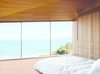 Modern home with Bedroom, Bed, and Light Hardwood Floor. The couple, both surfers and beach lovers, wake up to stunning views of the azure-blue Southern Ocean in their otherwise monochromatic eucalyptus master bedroom. Wardle’s firm designed the bed base, and the panel in the ceiling hides a television. Photo of Our Favorite Bedrooms