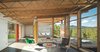 Modern home with Living Room, Chair, Coffee Tables, Floor Lighting, Lamps, and Rug Floor. The architects wrapped the glazing around the corner of the living room to bring the landscape inside. The open-web trusses run continuously from indoors to out. A fleet of Modernica furnishings complement a Prototype Boomerang chair by Richard Neutra, a custom Moufelt industrial felt rug, and Circa50 butterfly chairs. Photo of Eames Molded Chairs