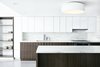 Modern home with Kitchen, White Cabinet, Marble Counter, and Ceiling Lighting. In the sleek kitchen, the white Ikea cabinet uppers seem to disappear into the wall, while the bases get a distinctive custom walnut wrapping. Flanking the cabinets are open bookshelves, which provide secondary function as a spacial divider for the children’s play area. A Dornbracht faucet sits on a slab of Vermont Olympian White Danby marble, which is also used for the island and backsplash. Photo of Ever Dream of Taking Over Your Neighbor’s Apartment?