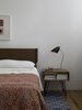 Modern home with Bedroom, Bed, Night Stands, and Table Lighting. The second-floor master bedroom, originally a science classroom, is now the owners' favorite parts of the home. “Before the renovation, our bedroom was very small and somewhat dark. It's now filled with light and quite spacious,” says resident Susan Hashemi. Rich wood furnishings include Design Within Reach bed and From the Source tables. The maple floors, original to the schoolhouse, have naturally patinated over time. A David Weeks Studio bedside lamp and geometric Madeline Weinrib rug accent the space. Photo of Ever Dream of Taking Over Your Neighbor’s Apartment?