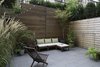 Modern home with Outdoor, Back Yard, Small Patio, Porch, Deck, Tile Patio, Porch, Deck, Hanging Lighting, and Horizontal Fences, Wall. The living room leads to a private outdoor patio. Before the renovation, the slightly below grade area was in plain sight to passersby, as it lays adjacent to the public walkway into the building. This less-than-ideal setup was addressed in the redesign by adding a slatted cedar perimeter fence, along with tall trees and shrubs. Clever hidden doors conceal patio storage under the entry walkway. Photo of Ever Dream of Taking Over Your Neighbor’s Apartment?