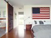Modern home with Bedroom, Medium Hardwood Floor, and Bed. He built the walnut bed and nightstands in the master bedroom with the help of Hannah’s two brothers. One of his clients at his hair salon gave him the American flag; the bedside lights are Tolomeo classic wall lamps by Artemide. The bed linens are
from Inhabit. A sliding barn door rolls sideways to reveal the bathroom. Photo of Material Focus: Custom Walnut Designs
