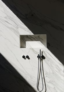 A shaft of sunlight streams into the marble shower, through a glass atrium that connects the master suite to the outdoors while maintaining privacy; the fixtures are by Vola.