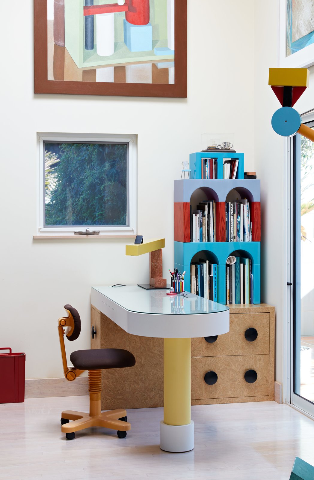 Office, Study Room Type, Storage, Chair, Desk, Light Hardwood Floor, and Bookcase Giotto shelves, a Treetops floor lamp, and an Olivetti chair—all by Sottsass—furnish the home office. Adrian designed the desk, and the painting is by Nathalie Du Pasquier, one of the original Memphis designers.