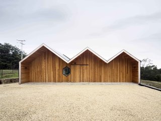 Crump played with the traditional gable roof form common to Australian farmhouses and transformed it into something entirely modern. The house’s three distinct ridgelines follow each other in succession, their simple contours conjuring a cartoon lightning bolt. The wood cladding covering the exterior also lends the house an impenetrable feel, heightening the surprise visitors experience upon entering and seeing its open, seaside views.