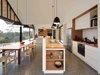 Modern home with Kitchen, Wood Counter, White Cabinet, Pendant Lighting, Range, Terrazzo Floor, Wall Oven, Refrigerator, Drop In Sink, and Subway Tile Backsplashe. The dining room is delineated from the kitchen by a long kitchen island with a higher partition between the two spaces. The island provides storage along its length, with exposed shelving at the ends. The drum lighting pendants by Axiom were also made using local timber. Photo 5 of Lookout House