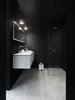Modern home with Bath Room, Concrete Floor, Wall Mount Sink, Wall Lighting, Enclosed Shower, and Corner Shower. The bathroom includes a stainless steel-and-aluminum Vipp bath module with integrated sink, faucet, and Corian countertop; Vipp spot lamp; glass-walled shower with a complete set of Vipp bathroom accessories; towels; and a Duravit toilet. Photo of Prefab Gets a Makeover With Danish Industrial Design