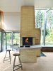 Modern home with Kitchen and Concrete Counter. The open-plan home’s core is the towering chimney—clad in the same double-long, thin bricks that sheathe the Kolumba museum in Cologne, Germany. It holds three fireplaces, a conventional oven, and a pizza oven; all vent into three distinct flues, emerging from the chimney as their own kind of architectural statement. Inside, life revolves around the brick chimney, which the architect surrounded with a concrete counter that wraps from the kitchen to the living area. The stools are vintage. Photo of Cozy Fireplaces