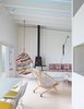 Modern home with Living Room, Wood Burning Fireplace, Wall Lighting, Bench, Ottomans, Chair, and Coffee Tables. Alexandra Angle transformed a beachside cabin into a colorful retreat for a college friend and her family. The living area features a PP130 Circle Chair by Hans Wegner and a Shaker wood stove by Antonio Citterio with Toan Nguyen for Wittus. A Tropicalia Cocoon hanging chair by Patricia Urquiola complements the fabric from Liberty that Angle used for the cushions on the built-in banquette. Photo of Homes Filled with Colorful Furniture