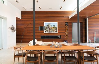 Ipe paneling and concrete floors continue into the living area, where a photograph by Scott McFarland hangs above the fireplace. Surrounding the dining table, by Riva 1920, are walnut chairs the couple found locally.