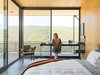 Modern home with Bedroom, Bed, Chair, Concrete Floor, Lamps, Shelves, and Table Lighting. Architect Bruce Bolander made the most of a limited footprint in a house he designed in a Malibu canyon. With the small bedroom unable to accommodate any "normal" size desk, the architect designed a very thin custom steel desk where resident Heidi Wright works. The floor-to-ceiling sliding glass doors from Metal Window Corporation open the entire corner of the room up to the outdoors. “The mountains across the way are almost like another wall—they contain the space to the point that you feel like you’re in a much bigger space, that you’re part of the overall landscape,” says Bolander. Photo by J Bennett Fitts. Photo of Our Favorite Bedrooms