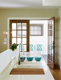 A large, white porcelain sink is complemented by a more sculptural, off-center faucet with an integrated sprayer.