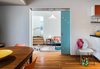 The programming of the garage addition called for a secondary living space and laundry room downstairs, new work spaces for both Eliza and Anthony upstairs, and a master suite. “My favorite parts of the home,” says Eliza, “are the ways in which it’s both spacious and open, and yet also allows you to close off sections of the house from other sections. The kids can be running around crazy downstairs and you can be upstairs and not hear a thing.”
Downstairs, the kitchen and dining room from the original home are linked to the new addition by pocket doors with the same color and motif as the front entry door. Both doors are dotted with clear plexiglass rods in a diagonal pattern. The new living space features a Bensen sofa, Crate & Barrel Ditto Cube table, and Luceplan Agave ceiling light fixture. Photo 4 of An Eye-Catching San Diego Addition with a Curved, Two-Story Garage Door modern home