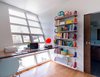 Eliza, a writer, and Anthony, a music professor, both gained new office spaces. Eliza’s office is positioned against the angled storefront window, with a custom, site-built writing desk. The slant of the garage addition serves an aesthetic and functional purpose: in addition to being visually dramatic and eye-catching, the curve enables more interior volume without occupying a larger footprint. Adjustable shelving by ISS and colorful clip-on bookends from Vernon Library Supplies complete the space. Photo 5 of An Eye-Catching San Diego Addition with a Curved, Two-Story Garage Door modern home