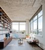 Modern home with Living Room, Coffee Tables, Chair, Sofa, Bookcase, Storage, Shelves, Media Cabinet, Lamps, Medium Hardwood Floor, and Floor Lighting. The windows on the right look out to Manhattan. The blue Acapulco chair echoes the aquatic tones of the bathroom tiles. Photo of Brooklyn Loft Renovation Masters Storage with a Custom Cabinet Wall