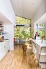 Modern home with Kitchen, White Cabinet, and Light Hardwood Floor. Sarah Magill and Copa, her golden retriever, relax in the kitchen of her home in Kansas City, where an eco-quartz-topped island can be used as a dining table—one of the home’s many adaptable features. The Akurum cabinets and handles are from Ikea, as are the Franklin folding bar stools, and the appliances are compact models from Summit. Photo of Architects Get Crafty With Budgets to Build Cost-Effective Modern Homes