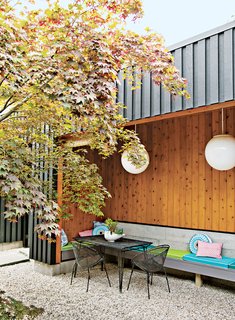 In the gravel-lined entry court shaded by a Japanese maple tree, furniture from Beall and Bell—an antique shop in Greenport, New York—mixes with Pendant Globes by Primelite Manufacturing. Bobo pillows by Adler outfit the banquette, and cedar clads the interior of the seating area.