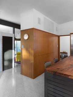 A new pantry wall in a teak wood veneer supplies all-but-invisible cabinet space with the help of touch-latch door hardware. Perched atop the existing terrazzo flooring, the underbelly of the kitchen's central island, painted with Benjamin Moore paint in the Midsummer Night shade, is visible beneath the reclaimed American elm countertop.