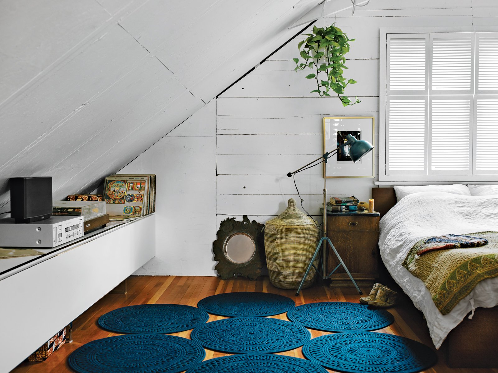 In the bedroom, a light by Bretford in Chicago is next to an Ikea Malm bed topped with Indian linens and folk weavings. The rug is from Paola Lenti. A Bocci 19 brass bowl sits near a hamper from Connected Fair Trade Goods.