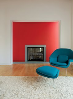 In the living room, Fashandi enjoys lounging in the Saarinen Womb chair by Knoll near the fireplace. The red wall is flanked by thin windows, causing it to glow in the sunlight.