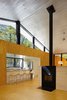 A Rais wood-burning fireplace heats the central space and the architectural element surrounding it was designed and installed by Charlie Lazor. The sleek, minimalist kitchen is outfitted with zinc countertops and the counterstools are by Blu Dot. Photo of Superior Logic modern home