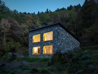 The positioning of the home’s roof allowed for a double-height, north-facing wall with four matching windows and an accompanying skylight. “The house refers to rural houses: a sloping roof, completely coated by stone and with no eaves,” Vanotti says.