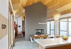 The home primarily features two materials: tile and wood. In between the dining room and living room, a fireplace is wrapped in floor tiles of a similar color to those lining the ground. Above, Douglas Fir plywood lines the ceiling. Rendely wanted a ceiling that had a rustic, distinctively non-urban look to it, and everyone agreed a wooden ceiling would make the space feel more cozy. Photo 3 of The Farm modern home
