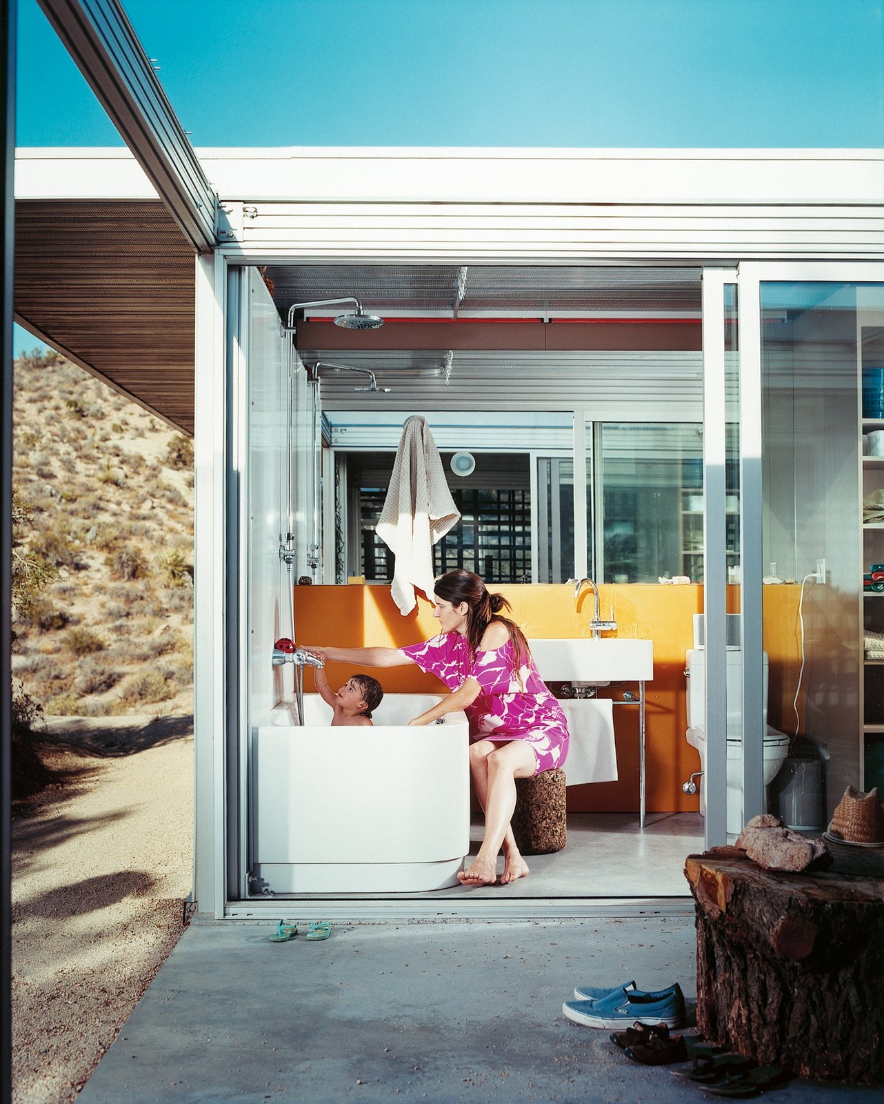 Linda Taalman and Alan Koch, of Taalman Koch Architects, completed work on their glass iT House, a lovely, minimal home that tests the limits of living lightly on the land in the desert near Joshua Tree National Park. The bath and basin in the bathroom are by Duravit, and the orange wall is by Three Form.