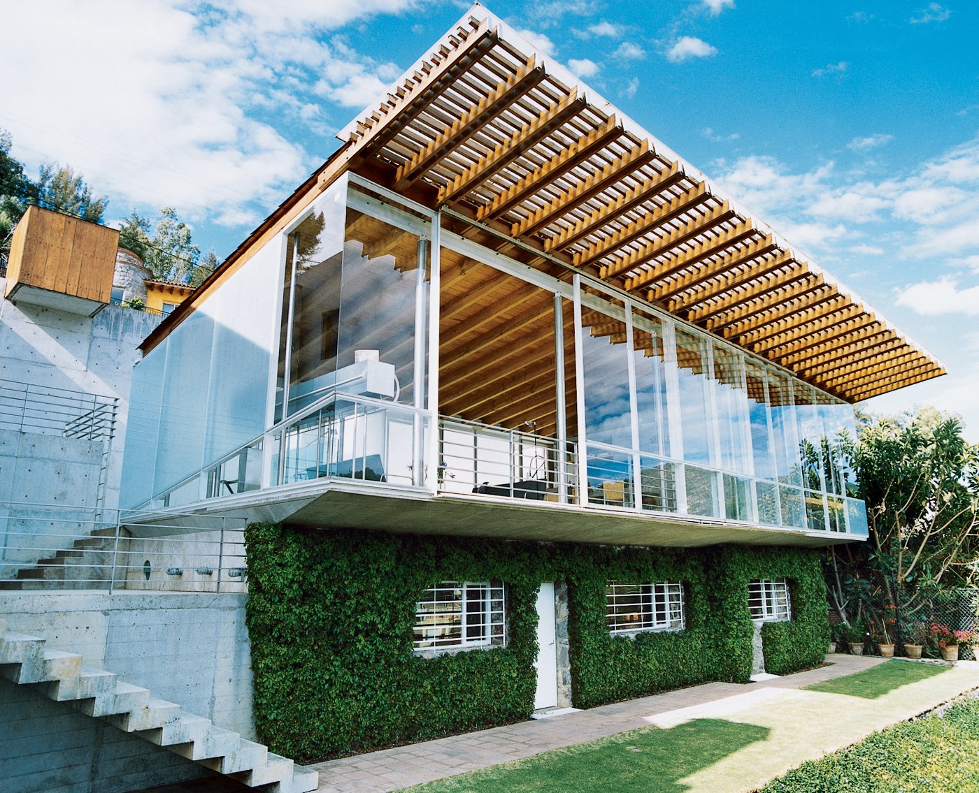 The house has what some architects would call an upside-down plan, with living spaces upstairs and bedrooms below. The upper story is strikingly transparent; the lower is camouflaged by thick, foliage-covered walls, which keep the sleeping areas cool.