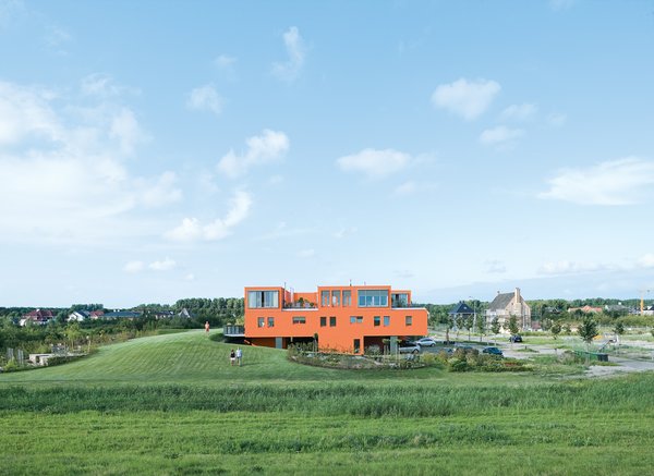 Seen here from the south, Villa van Vijven’s orange facade is meant to mimic the tiled rooftops of Holland’s country buildings, while the building’s horizontal pull echoes the flat landscape. The second-floor living rooms look out on the 4,200-square-foot communal garden, one of only two shared spaces in the whole community. Bob Krone, Koos Sweringa, and Marianne Schram stroll the grounds.