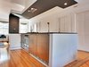 Chris's original design consisted of only the island, which houses two Fisher Paykel dish drawers as well as a 24-inch gas oven and cooktop and two under-counter fridges by De'Longhi. Danielle, however, urged him to create a framed kitchen area so the living room on one side (shown here in the background) and the dining room on the other wouldn't bleed into each other as a single space. "That's how the canopy was born," Chris says. In addition to semi-enclosing the kitchen with the lowered, painted ceiling and partial wall, the canopy hides structural elements and the Broan hood for the cooktop. Photo by Kate McElwee. Photo of D House Kitchen Renovation modern home