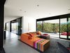 Modern home with Living Room, Concrete Floor, Sofa, and Recessed Lighting. The Mikado 2 sofa by Hans Hopfer for Roche Bobois is a bright and cheery centerpiece in the otherwise sedate living room. The nubby wool Photon rug from Design Within Reach warms up the expanse of concrete. The framed drawing is by the Los Angeles–based artist Daniel Brice. Huge sliding doors open the house to the outdoors and virtually double the Burtons' living space. Photo of How to Design with Orange