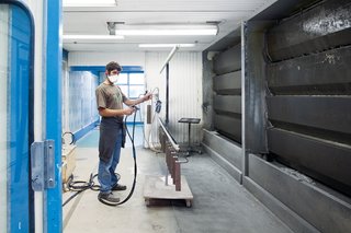 A technician in a ventilator mask who sprays the wood with a transparent stain or varnish.