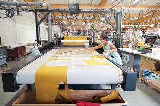 A seamstress mans the automated Gerber Cutter, which cuts patterns precisely and in a way that minimizes wasted fabric.