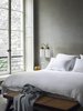 Modern home with Bedroom, Bench, Bed, and Wall Lighting. Architect Joseph Dirand's bedroom boasts sandy gray walls and upholstered headboard. The white bed linens help reflect daylight into the space and the Azucena sconces offer task illumination. Photo of Monochromatic Color Palettes Are the Ultimate Modern Design Tool