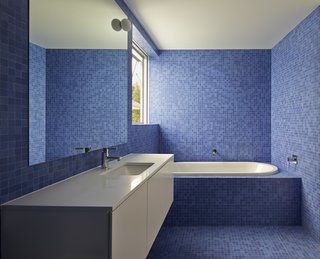 This bathroom, tiled in bright blue mosaic to offset the home’s limited materials and color palette, calls for a simple vanity. The sinks, toilets, and tubs are by Villeroy & Boch, while the faucets and towel rails are by Grohe and Avenir, respectively. 