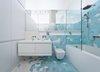 Modern home with Bath Room, Wall Mount Sink, Alcove Tub, Ceramic Tile Floor, Ceramic Tile Wall, One Piece Toilet, and Open Shower. The bathroom, located just adjacent to the kitchen, features a pattern of gray and turquoise tiles that climbs from the floors up the walls. They serve as a burst of color among the predominately white walls elsewhere, transforming the bathroom into one of the apartment’s most striking spaces. Photo of Brooklyn Loft Renovation Masters Storage with a Custom Cabinet Wall