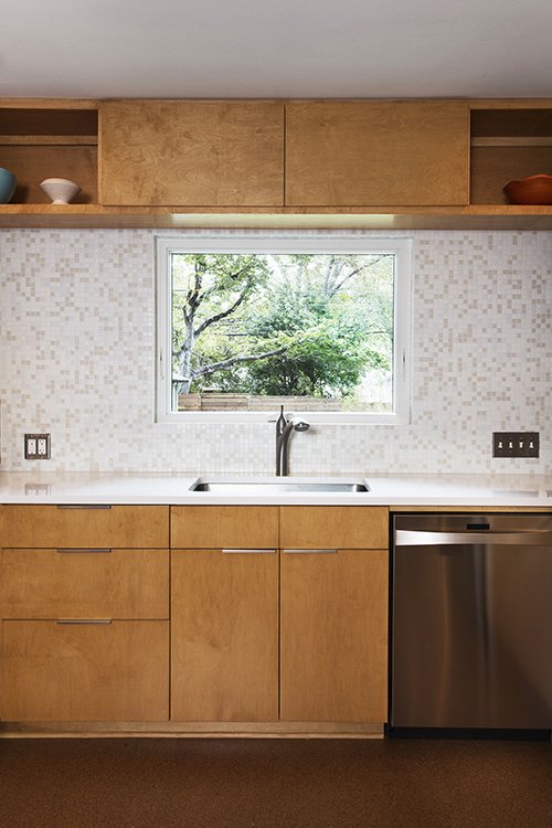 Owners Kirsten and Lloyd chose a muted mosaic tile from Modwalls to cover the backsplash and back wall of the kitchen. New cork floors from House + Earth give a nice feel underfoot. Perforated chrome lights from Rejuvenation under the bar soffit enhance the mid-century vibe.