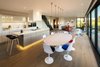 A white marble dining table and matching plastic chairs sit beneath copper pendants with Plumen light bulbs. On the other side of the open-plan living area, the sofa, table, and chairs, which predate the house, are perfectly integrated with their new surroundings. Photo 4 of Sandpath modern home