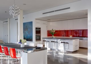 Though the home’s common areas are largely white and monotone, the kitchen introduces a pop of red, the owner’s favorite color, through the glossy AGC kitchen backsplash. Stone pietra cardosa counters are used on the center island, along with white Corian around the perimeter. A Miele range, Sub-Zero refrigerator, and Piston stools by Shin and Tomako Azumi complete the space.