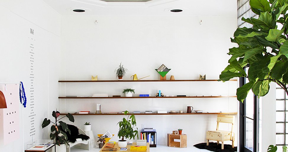 Various goods hang out on long wooden shelves mounted on the wall with plenty of natural light infiltrating in to the right. Photo via Table of Contents.