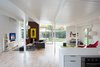 Modern home with Living Room, Bench, Chair, Sofa, Ottomans, Media Cabinet, Floor Lighting, Bookcase, Light Hardwood Floor, Pendant Lighting, and Standard Layout Fireplace. The living spaces of house, built in 1972 or 1973, were originally divided into three—a kitchen, living and dining area, and an atrium (previous owners had covered the atrium with a roof). "The new owners wanted the interior space to flow as one, so we removed the glass doors and solid walls separating the enclosed atrium from the kitchen and living room," principal John Klopf says. "Some structural posts needed to remain to hold up the roof, but overall the space was opened up almost completely. The floor was leveled, and the plan freed up." The rainbow print is a 1960s Herman Miller trade poster, and the Vitamin Water print by a New York artist. A Sapien book tower from Design Within Reach sits next to the TV. The sofa is IKEA. Photo of Modern Master: Joseph Eichler