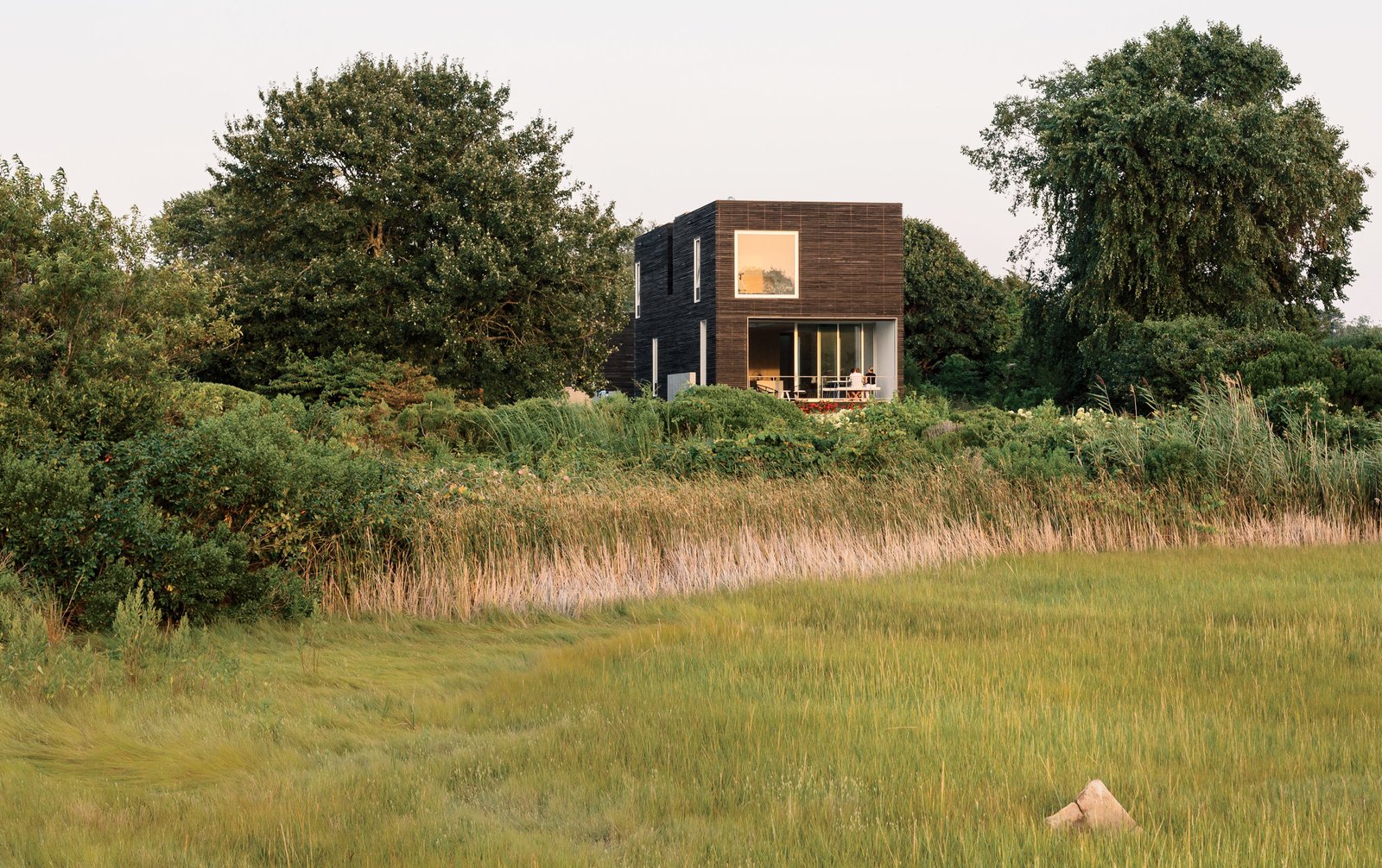 Native New Yorkers, the Merola family have long held a tradition of spending summers in Rhode Island. When they learned the costs of renovating their existing cottage would significantly outweigh the benefits, they instead opted to build new. The result—a distinctively modernist box structure clad in milled slats of charred, brushed, and oiled cypress manufactured by Delta Millworks—sits nestled within the marshy landscape of Quonochontaug Pond.