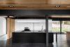 Modern home with Kitchen, Wood Backsplashe, Cooktops, Granite Counter, Dark Hardwood Floor, Refrigerator, White Cabinet, Pendant Lighting, Accent Lighting, Wall Oven, and Undermount Sink. A dramatic black island is expertly balanced by a wall of white cabinetry and a refrigerator that blends perfectly. The kitchen’s black countertops were cut from Nero Assoluto granite. The sink and faucet are from Quebec-based company Rubi. Appliances are from Wolf. Photo 5 of The Phoenix