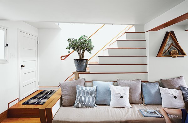 Owner-architect Lyle Bradley moved the stairs in his home against a party wall, and a new skylight above the staircase now bathes both floors in natural light. In the living room, the stair's lower step reaches out to form an arm, while the ascending stairs create a natural incline for cushions. 