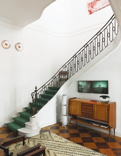 At a design-focused mansion in Belgium, the soaring atrium is home to a jacaranda high board from the 1960s, a chrome and glass lamp from Italy, a black leather chair and footstool by Sergio Rodrigues, a Berber rug, and a pair of photographs by the Brazilian artist Luiz Braga.