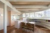 The kitchen and dining area features an integrated system by LIXEL, a custom-made table, and Tendo chairs. A bespoke, curved bookshelf wraps around the wall beneath a panoramic window. Photo 5 of Half & Half House modern home